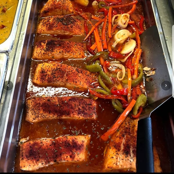 Baked salmon fillets with bell peppers, onions, and carrots in a rich sauce, ready to serve.