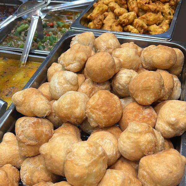Close-up of golden-brown Caribbean fried dumplings, with other dishes blurred in the background.