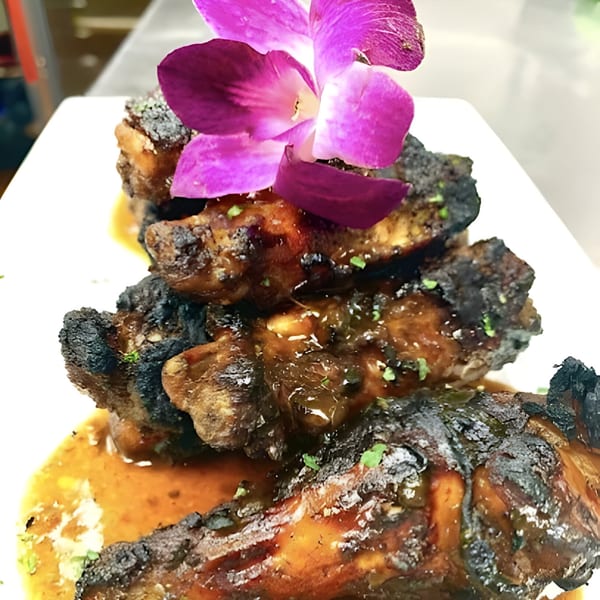 Island Crave's jerk chicken wings, glazed and garnished with a vibrant purple orchid.