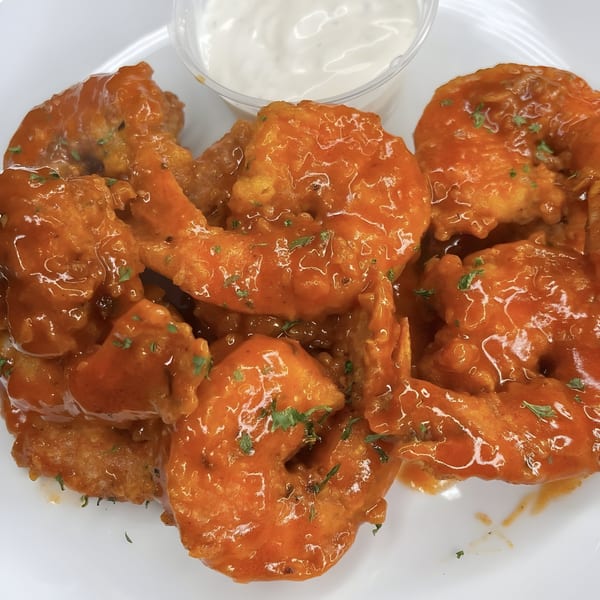 Island Crave's Caribbean-style shrimp, coated in a vibrant orange sauce and garnished with herbs, served with a side of white dipping sauce.