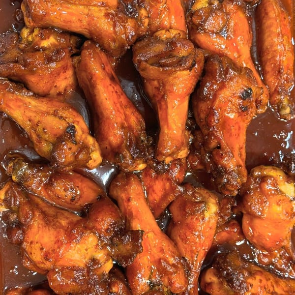 Close-up of numerous glistening Caribbean jerk chicken drumettes and wings in a rich, dark sauce.