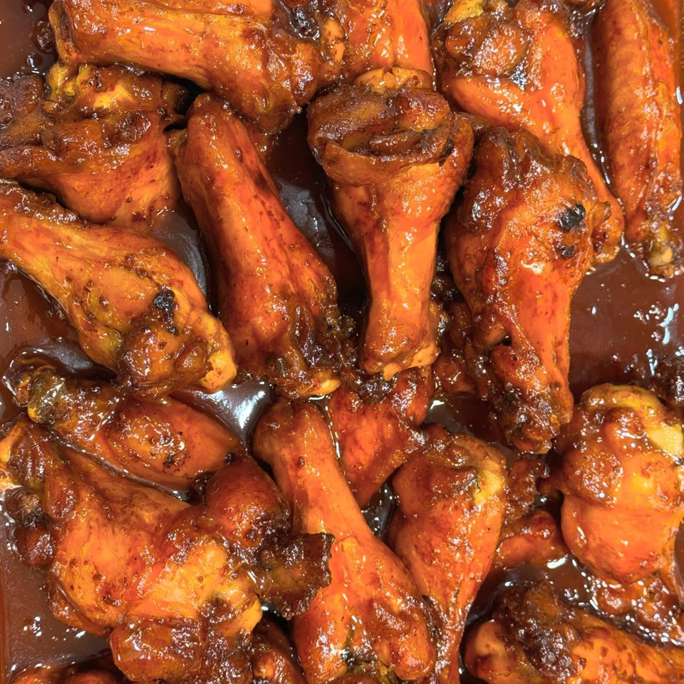 Close-up of numerous glistening Caribbean jerk chicken drumettes and wings in a rich, dark sauce.